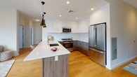 Located at 703 Whitney Ave in New Haven, CT, this contemporary 2-bedroom, 2-bathroom residence offers a thoughtfully designed single-floor layout that blends modern aesthetics with everyday functionality. The open-concept living, dining, and kitchen area is anchored by warm hardwood floors, recessed lighting, and a skylight that floods the space with natural light. Large windows frame neighborhood views and enhance the bright, airy ambiance throughout.

The kitchen is a standout feature, showcasing sleek two-tone cabinetry — white uppers paired with wood-grain lowers — a generous island with a white quartz countertop and undermount sink, stainless steel appliances, and striking black pendant lights. The living area offers a clean, modern fireplace set into the wall, while the adjoining dining space accommodates a glass-top table and mid-century inspired seating.

Both bedrooms are calm and comfortable, dressed in soft blue-gray tones with hardwood floors and ample natural light from well-placed windows. The two bathrooms reflect refined design: one features large-format stone-look tile, a floating vanity, and a soaking tub, while the second offers a herringbone-patterned tile floor, a wood-tone vanity, and a walk-in shower. Every detail reflects a cohesive, contemporary vision.