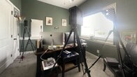 Located at 3216 NW 50th Terr in Riverside, Missouri, this single-room home office offers a focused and functional workspace designed for productivity. The room is defined by its distinctive sage green walls, which lend a calm, focused atmosphere to the space. Soft carpeted flooring adds warmth underfoot, complementing the room's cozy yet professional character.

A dedicated desk area serves as the centerpiece of the office, positioned near a window that allows natural light to fill the room and provides a view of the surrounding exterior. The window is fitted with a roller shade for light control. Built-in storage is provided by a set of white paneled double doors with matte black hardware, offering a clean, classic aesthetic that contrasts nicely with the green walls.

Wall-mounted framed artwork and credentials add a personal and academic touch to the space, contributing to the room's professional character. White painted trim and baseboards provide crisp definition throughout. A door with paneled detailing and matching black hardware connects the office to the rest of the home, with steps visible just beyond the threshold. The overall ambiance is intimate and purpose-driven, making this a well-appointed private office suited for focused, day-to-day work.