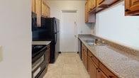 Located at 10398 Valley Forge Dr in Parma Heights, Ohio, this single-floor unit offers a clean, well-maintained interior with a cohesive design throughout. Light wood-style flooring runs through the main living areas and bedrooms, creating a bright and consistent aesthetic that pairs naturally with the crisp white walls found throughout the space.

The living room is an open, welcoming area featuring a large front-facing window fitted with vertical blinds that allow generous natural light, along with a wall-mounted air conditioning unit for climate control. A front entry door with a decorative half-moon transom window adds a subtle architectural detail to the entryway.

Adjacent to the living area, a dining space features vaulted ceiling lines and a pendant light fixture, transitioning into a tiled area that leads to the galley-style kitchen. The kitchen is efficiently laid out with warm wood cabinetry, granite-look countertops, a double sink, and black appliances including a refrigerator, range, and dishwasher, all set on light tile flooring.

The bedrooms are comfortably sized, each featuring the same light wood-style flooring, white walls, and ceiling fans with light fixtures. One bedroom includes a window with natural views.

The bathroom is well-appointed with a dark wood vanity, white countertop, a framed mirror, dark tile flooring, and a glass-enclosed shower stall.