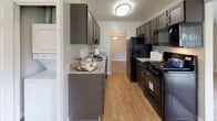This single-floor residence offers a well-organized layout with multiple rooms connected by a central hallway. The living area is generously sized, featuring plush wall-to-wall carpeting, neutral gray walls, and large sliding glass doors dressed with vertical blinds that invite abundant natural light and provide access to outdoor views. The space flows naturally into adjacent rooms, creating a cohesive and functional floor plan.

The kitchen is a standout feature, designed in a galley configuration with dark gray cabinetry, granite-look countertops, and black appliances including a gas range, refrigerator, and built-in microwave. Light wood-style flooring adds warmth and contrast to the darker finishes, while a flush-mount ceiling fixture provides practical illumination.

The bedrooms are carpeted in the same neutral tones found throughout the living areas, each featuring soft gray walls, white trim, and windows with blinds offering natural light. One bedroom includes a built-in window seat, adding a charming architectural detail. Closet space is also present.

The bathrooms are finished with light ceramic tile flooring, white fixtures, and chrome hardware, offering a clean and functional aesthetic. The layout as a whole presents a comfortable, move-in ready environment with consistent, neutral finishes throughout.