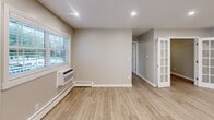 Located at 1710 Devonshire Rd in Hauppauge, NY, this thoughtfully updated 2-bedroom, 1-bathroom unit offers a clean, modern aesthetic throughout its efficiently designed single-floor layout. The open-concept kitchen and living area serves as the heart of the home, showcasing a striking granite-topped peninsula with an undermount sink, pendant lighting, white shaker cabinetry, and a full suite of stainless steel appliances including a gas range, microwave, and refrigerator. Light wood-style flooring runs throughout the main living areas, complementing the neutral gray wall palette and recessed lighting. The living room is generously proportioned, featuring a charming French door entry and a large window that invites natural light. Both bedrooms are carpeted for comfort and equipped with ceiling fans; the primary bedroom includes a wall AC unit and a bright window with exterior views. The full bathroom is finished with large-format tile surrounding a tub/shower combination, accented by a frosted glass window. A dedicated closet provides additional storage. The overall ambiance is fresh, clean, and move-in ready, reflecting contemporary updates with a functional, comfortable design.