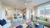 Located at 613 Meadowbrook Pkwy in Colorado Springs, CO, this well-appointed single-floor home offers a thoughtfully designed open-concept layout with contemporary finishes throughout. The heart of the home is a sleek kitchen featuring light gray cabinetry, a large center island with a built-in sink and dishwasher, stainless steel appliances, subway tile backsplash, and dramatic pendant lighting. The kitchen flows seamlessly into a bright living area, where large corner windows flood the space with natural light and offer views of the surrounding neighborhood. Wide-plank wood-style flooring and a ceiling fan add comfort and cohesion to the main living space. The bedrooms are carpeted and generously sized, with clean white walls and ample natural light. A walk-in closet with built-in shelving and hanging rods provides excellent storage. A full bathroom includes a tiled tub-shower combination and wood-style flooring. A standout feature is the built-in home office nook, complete with overhead cabinetry and a quartz desktop surface — ideal for working from home. The overall ambiance is modern and airy, combining functional design with stylish, curated details throughout every room.