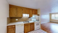 Located at 20 Park St in Lynn, MA, this two-bedroom, one-bathroom unit offers a practical and well-organized single-floor layout. The combined living and dining area serves as the heart of the home, featuring warm hardwood flooring, neutral cream-toned walls, and a large window with vertical blinds that invites natural light and outdoor views. Baseboard heating runs throughout, ensuring year-round comfort. The kitchen is efficiently designed with warm wood cabinetry extending to the ceiling for generous storage, white countertops, a tile backsplash, and a classic patterned vinyl floor. It is equipped with a gas range, dishwasher, and a stainless sink, with direct access to the main living area. Both bedrooms continue the hardwood flooring theme and feature large windows with vertical blinds, baseboard heating, and ample closet space — the unit includes four closets in total, providing excellent storage throughout. The primary bedroom is generously sized and includes its own wall-mounted air conditioning unit. The bathroom features a full tub-shower combination with clean white surrounds and tiled walls. A hallway connects the rooms efficiently, and the unit's entry opens directly into the kitchen area, adding convenience to the overall flow of the home.