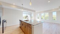 This well-appointed single-floor residence offers a thoughtfully designed open-concept layout that seamlessly connects the kitchen, dining, and living areas. The kitchen is a standout feature, anchored by a large center island with a granite countertop, an undermount sink, and pendant lighting overhead. Warm wood-toned cabinetry pairs with a classic white subway tile backsplash, and the space is equipped with a full suite of stainless steel appliances, including a gas range, microwave, and French door refrigerator. Light hardwood flooring flows throughout the main living areas, complementing the bright, neutral color palette. The spacious living area is bathed in natural light through a bank of large windows that frame lush tree-lined outdoor views. An in-unit washer is also visible, adding everyday convenience. The bedrooms feature plush carpeting and generously sized windows that continue the outdoor views and invite ample sunlight. The primary bathroom offers a dual-sink vanity with granite countertops, matching wood cabinetry, and a walk-in shower area, while the secondary bathroom includes a full tub-shower combination. Throughout the residence, the clean architectural lines, recessed lighting, and consistent finishes create a cohesive, modern ambiance.