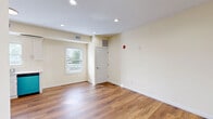This single-floor, 2-bedroom, 1-bathroom unit offers a clean and modern living environment with consistent warm-toned hardwood-style flooring running throughout every room. The open living area is bright and welcoming, featuring recessed lighting, neutral cream-colored walls, and a front entry door with adjacent window that allows natural light to filter in.

The kitchen is a functional standout, equipped with crisp white shaker-style cabinetry, ample upper and lower storage, and a full suite of stainless steel appliances including a gas range, over-the-range microwave, bottom-freezer refrigerator, and dishwasher. A window above the sink provides natural light to the workspace.

The primary bedroom is generously sized, offering a double-door closet and a window with views to the exterior. The second bedroom is well-proportioned and similarly bright with its own window. Both rooms maintain the consistent neutral palette found throughout the unit.

The bathroom is finished with large-format tile flooring, a tiled walk-in shower stall, a wall-mounted sink with medicine cabinet mirror, and a towel ring — all in a clean, minimal style. A hallway connects the main living areas to the bedrooms and bathroom, providing a logical and efficient floor plan layout throughout this thoughtfully designed space.