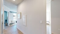 Located at 2050 W Ogden Ave in Chicago's West Side, this 3-bedroom, 2-bathroom unit showcases a striking industrial-modern aesthetic across a single thoughtfully designed floor. Soaring exposed concrete ceilings and visible ductwork lend an authentic urban character throughout, while light wood-tone flooring unifies the open-plan living areas with warmth and continuity.

The kitchen is a standout feature, outfitted with light wood cabinetry, stainless steel appliances, under-cabinet lighting, and a spacious white waterfall island with bar seating — ideal for both cooking and casual dining. The living area flows seamlessly from the kitchen and opens to a private balcony through full-height glass doors, inviting natural light and outdoor views into the space.

Two well-lit hallways connect the bedrooms and bathrooms, maintaining a clean, organized layout. The primary bedroom features a built-in closet and exposed concrete ceiling details, while an additional bedroom benefits from floor-to-ceiling windows with city views. Both bathrooms are finished to a high standard, featuring marble-look tile flooring, wood-toned vanities with matte black hardware, illuminated mirrors, and glass-enclosed showers. The overall ambiance is clean, contemporary, and purposefully designed.