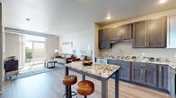 Located at 412 3rd St E in Hastings, MN, this 2-bedroom, 2-bathroom residence offers a thoughtfully designed open-concept layout. The kitchen is a standout feature, showcasing rich dark-stained cabinetry, granite countertops, stainless steel appliances, and a center island that provides additional prep space and seating. The kitchen flows seamlessly into the living area, which is finished with light wood-style flooring and floor-to-ceiling sliding glass doors that open to a private balcony, flooding the space with natural light and offering pleasant views of the surrounding greenery. An exposed duct detail adds an industrial design touch to the living area. Both bedrooms are carpeted for comfort, with neutral tones and windows that bring in natural light. The primary bedroom includes a walk-in closet equipped with wire shelving systems and direct access to an en-suite bathroom featuring a wide granite-topped vanity with dark cabinetry and a well-lit mirror. The second bathroom includes a clean, walk-in shower with chrome fixtures. Two dedicated closets provide ample storage throughout the unit. The consistent use of granite surfaces, dark wood cabinetry, and light flooring creates a cohesive, modern aesthetic throughout.