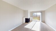 Located at 14095 SW Walker Rd in Beaverton, Oregon, this single-floor residence offers a thoughtfully laid-out living space with a neutral color palette and practical finishes throughout. The living room serves as the centerpiece of the home, featuring plush carpeting, a textured ceiling, and a freestanding fireplace with a tiled surround. A sliding glass door floods the room with natural light and opens directly onto a wood-railed balcony overlooking a green outdoor setting. A ceiling fan provides additional comfort in the adjoining area, which connects seamlessly to the kitchen. The kitchen is well-equipped with white cabinetry, dark countertops, a double-basin sink, a white range, and a dishwasher. Light tile flooring and a window with blinds complete the space, keeping it bright and functional. A hallway connects the main living areas to the private spaces, including a full bathroom appointed with tile flooring, a vanity with dark countertop, and a full tub and shower combination with a curved rod and grab bar. Carpeted throughout the bedrooms and main living areas, the residence offers a comfortable and cohesive feel. The layout is efficient and well-organized, making excellent use of available space across its single floor.