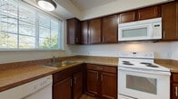 Located at 1204 Sherwood Ct in Rochester Hills, MI, this multi-level home spans three floors and offers a well-organized layout with a variety of functional living spaces. The kitchen is outfitted with rich dark wood cabinetry, granite-style countertops, hardwood flooring, and white Whirlpool appliances including a range, over-the-range microwave, and dishwasher. A window above the sink fills the space with natural light. The dining area features plush carpeting and a sliding glass door that opens to an outdoor balcony, complemented by an elegant chandelier overhead. The spacious living room continues the carpeted flooring and connects seamlessly to the rest of the main level. The bedrooms are carpeted and bright, each featuring ceiling fans and windows that invite natural light. One bedroom includes a generous walk-in closet with built-in shelving. The full bathroom is finished with large-format tile flooring, a combined tub and shower, and a dark wood vanity with a stone-style countertop. The unfinished basement level offers substantial open space with painted concrete floors, exposed structural framing overhead, and small windows that provide ventilation and light — presenting excellent potential for future customization or storage use.