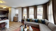 This well-appointed single-floor residence offers a cohesive blend of modern finishes and comfortable living spaces throughout. The open-concept kitchen is a standout, featuring rich dark cabinetry that extends to the ceiling, light quartz countertops, a subway tile backsplash, stainless steel appliances including a full-size refrigerator and range, and a large central island with a double sink — ideal for both cooking and entertaining. Wood-look flooring flows through the kitchen and bathrooms, adding warmth and continuity.

The living area is generously sized and bathed in natural light through a bank of large windows dressed with floor-to-ceiling drapes, creating an inviting and airy atmosphere with views to the outdoors. Two well-proportioned bedrooms each feature plush carpeting, ceiling fans with integrated lighting, and ample window coverage for natural light. The primary bedroom includes a striking large-scale wall mural, lending an artistic focal point to the space.

Both bathrooms are finished with dark wood vanities, quartz countertops, and wood-look tile flooring. One bathroom offers a soaking tub with a decorative shower curtain, while the other features a sleek walk-in glass shower and direct access to a walk-in closet, enhancing everyday functionality and convenience throughout.