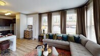 This well-appointed single-floor residence offers a cohesive blend of modern finishes and comfortable living spaces throughout. The open-concept kitchen is a standout, featuring rich dark cabinetry that extends to the ceiling, light quartz countertops, a subway tile backsplash, stainless steel appliances including a full-size refrigerator and range, and a large central island with a double sink — ideal for both cooking and entertaining. Wood-look flooring flows through the kitchen and bathrooms, adding warmth and continuity.

The living area is generously sized and bathed in natural light through a bank of large windows dressed with floor-to-ceiling drapes, creating an inviting and airy atmosphere with views to the outdoors. Two well-proportioned bedrooms each feature plush carpeting, ceiling fans with integrated lighting, and ample window coverage for natural light. The primary bedroom includes a striking large-scale wall mural, lending an artistic focal point to the space.

Both bathrooms are finished with dark wood vanities, quartz countertops, and wood-look tile flooring. One bathroom offers a soaking tub with a decorative shower curtain, while the other features a sleek walk-in glass shower and direct access to a walk-in closet, enhancing everyday functionality and convenience throughout.