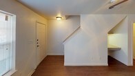 This two-story residence is organized across two well-defined levels connected by a staircase that is visible from the entry foyer. The ground floor welcomes occupants through a front door that opens into an entryway with warm hardwood-style flooring, which continues throughout the main living areas. The living room is a spacious, open area outfitted with a ceiling fan and light fixture, offering a bright and functional space. A pass-through opening connects the living area to the kitchen, which features dark espresso-toned cabinetry, granite-style countertops, hardwood-style flooring, and white appliances including a range and refrigerator. A full bathroom on this level includes a vanity with dark cabinetry, a granite-style countertop, and a tub-shower combination. The upper level houses the bedrooms, each finished with neutral-toned carpet, ceiling fans with light kits, and windows that allow natural light. One bedroom features vaulted ceilings, adding a sense of openness. A second full bathroom upstairs mirrors the design of the lower bath, maintaining consistent finishes throughout. The overall aesthetic is clean and cohesive, with a neutral color palette across both floors.