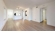 This single-floor residence offers a clean, modern aesthetic defined by crisp white walls, light hardwood-style flooring, and an open, airy layout that connects the main living and dining areas seamlessly. The spacious living room is filled with natural light and provides direct access to an outdoor area through sliding glass doors framed by vertical blinds, creating a bright and welcoming atmosphere throughout.

The kitchen is thoughtfully designed with a curved peninsula breakfast bar that opens to the living space, white shaker-style cabinetry, light quartz countertops, a white subway tile backsplash, and a full suite of stainless steel appliances including a refrigerator, electric range, and over-the-range microwave. A skylight above the kitchen floods the space with additional natural light. Light tile flooring grounds the kitchen area.

A dedicated in-unit laundry closet with a stacked washer and dryer unit adds everyday convenience to the living area. The bedrooms are generously sized with continued hardwood-style flooring and access to additional rooms. The bathroom features a white vanity with quartz countertop, an undermount sink, and a mirrored medicine cabinet. The textured ceilings and recessed track lighting throughout complete the well-maintained, move-in-ready presentation of this residence.