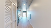 Located in Chicago's vibrant West Loop neighborhood, this one-bedroom, one-bathroom unit at 225 N Elizabeth St offers a thoughtfully designed modern interior with an industrial edge. The exposed concrete ceiling is a defining architectural feature throughout the space, complementing the light-toned hardwood flooring that runs underfoot. The open-concept living and kitchen area is anchored by a sleek kitchen fitted with dark upper cabinetry, stainless steel appliances including a dishwasher, a subway tile backsplash, and a modern faucet — all designed for both function and style. Floor-to-ceiling windows in the living area frame sweeping elevated views of the Chicago skyline and surrounding cityscape, flooding the space with abundant natural light. The bedroom is a clean, minimalist retreat with light wood flooring, crisp white walls, and a built-in closet with contemporary black hardware. The bathroom continues the modern aesthetic with large-format tile flooring, a glass-enclosed walk-in shower, a floating dark vanity topped with a white countertop, and a backlit vanity mirror that adds a polished finishing touch. A hallway with louvered storage doors connects the rooms efficiently, completing this well-appointed urban residence.