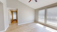 This single-story, 2-bedroom, 1-bathroom residence offers a thoughtfully arranged layout that makes efficient use of its space. The living area features light hardwood-style flooring, vaulted ceilings, a ceiling fan, and large windows dressed with horizontal blinds that invite generous natural light throughout the day.

The kitchen is designed with functionality in mind, showcasing gray cabinetry, a white countertop peninsula with an undermount sink, stainless steel appliances including a range, over-the-range microwave, and refrigerator, as well as recessed and overhead lighting. The open peninsula connects the kitchen to the living area, creating a cohesive, open feel.

The primary bedroom is a well-proportioned retreat with vaulted ceilings, a ceiling fan, light hardwood-style flooring, and large windows for ample natural light. The second bedroom features plush carpeting, a ceiling fan, a closet, and a bright window. Both bedrooms offer a comfortable and private atmosphere.

The bathroom includes a wide vanity with gray cabinetry, white countertops, and a large framed mirror. Hardwood-style flooring carries through the bathroom, maintaining visual consistency with the rest of the home. A hallway and dedicated closet round out this well-organized and move-in-ready residence.
