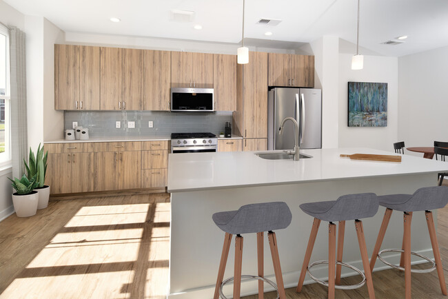 Upgrade Scheme townhome kitchen and dining areas with oak cabinetry, grey tile backsplash, grey quartz countertops, stainless steel appliances, and hard surface flooring - Avalon Old Bridge