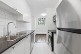 Located at 80 Cosburn Ave, Unit 406 in Toronto's East End, this one-bedroom, one-bathroom unit offers a well-organized layout across a single floor. The space is thoughtfully designed with clean white walls and warm parquet wood flooring that flows throughout the living and sleeping areas, adding a classic character to the interior.

The kitchen is a functional galley-style space featuring crisp white shaker cabinetry that extends to the ceiling for ample storage, dark countertops, a subway tile backsplash, a stainless steel sink, and modern stainless steel appliances. The kitchen leads directly to the unit's entrance, creating a practical and connected flow.

The bedroom is a comfortable, well-proportioned room finished with the same parquet flooring. A window overlooks mature trees, allowing natural light to filter in while offering a pleasant green view. A baseboard heating unit runs along the exterior wall, ensuring warmth throughout cooler months. The room also features a sliding closet door, maximizing usable space.

The bathroom is finished with bright white subway tiles surrounding a full-sized soaker bathtub and shower combination, complemented by chrome fixtures, lending a clean and timeless aesthetic. Overall, the unit presents a bright, practical, and move-in ready living space in a desirable Toronto neighbourhood.