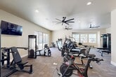 Located at 3100 N Akers St in Visalia, CA, this fitness center offers a comprehensive, single-level layout designed to support a wide range of workout routines. The facility is divided into two connected zones, providing dedicated areas for both cardio and strength training as well as functional fitness.

The main workout area is generously sized and flooded with natural light through large sliding glass doors and multiple windows, offering views of the surrounding outdoor area. Oversized ceiling fans are distributed throughout, ensuring consistent airflow across the space. The room is outfitted with an array of cardio equipment, including treadmills, ellipticals, stair climbers, a rowing machine, and Peloton cycling bikes. Strength training is supported by a cable machine, adjustable bench, and a full dumbbell rack, complemented by a large wall mirror that enhances the sense of space.

A separate functional training studio features TRX suspension trainers, kettlebells, medicine balls, and plyometric equipment, all set on patterned carpet tile flooring. Glass partition walls and doors connect this studio to the main floor, maintaining visual openness between the two areas.

A light-filled flex room with sliding glass doors opens to an outdoor terrace, offering a versatile space for stretching or group classes. A corridor leads to restroom facilities, completing this well-appointed fitness destination.