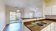 This single-story, 3-bedroom, 2-bathroom home offers a thoughtfully designed layout that balances comfort and functionality. The interior is unified by warm hardwood-style flooring in the main living areas and a neutral color palette that enhances the bright, airy atmosphere throughout.

The open-concept kitchen is a practical centerpiece, featuring white cabinetry, dark speckled countertops, a double-basin stainless steel sink, and white appliances including an electric range, over-the-range microwave, and a side-by-side refrigerator with an ice and water dispenser. A peninsula counter connects the kitchen to the living and dining areas, which are illuminated by pendant and ceiling fan lighting and benefit from sliding glass door access to the outdoors.

A central hallway, accented with crown molding, connects the home's three bedrooms. Each bedroom is carpeted and equipped with a ceiling fan, and features windows that invite natural light and outdoor views. The spacious primary bedroom is accompanied by a well-appointed en-suite bathroom with a long dual-sink vanity, a tiled soaking tub, and separate water closet. A large walk-in closet with wire shelving provides ample storage. The second bathroom is equally well-finished with hardwood-style flooring and a clean, neutral design. Three closets throughout the home ensure plentiful storage options.