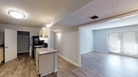 This single-story residence offers a practical and well-designed layout across two bedrooms and two bathrooms. The kitchen serves as a central feature, equipped with light wood cabinetry, granite-style countertops, black appliances including an electric range and stainless steel refrigerator, and a dedicated walk-in pantry for additional storage. A peninsula counter connects the kitchen to the adjacent living areas, which are finished with durable wood-look flooring throughout. The main living space benefits from natural light streaming through French doors that open to an outdoor area, creating a bright and inviting atmosphere.

Both bedrooms are finished with neutral-toned carpet and feature windows dressed with blinds that allow for natural light while maintaining privacy. The rooms offer generous wall space suitable for varied furniture arrangements. Each of the two bathrooms includes a full tub-shower combination with a white surround. One bathroom features wood-look flooring, a large mirror, and a vanity light fixture. Textured ceilings are consistent throughout the unit, and neutral gray wall tones provide a cohesive, move-in-ready aesthetic across all rooms.