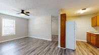 Located at 119 Waverly Way in Carrollton, GA, this single-floor unit offers a practical and efficient layout designed to maximize every square foot. The combined kitchen and living area serves as the heart of the space, featuring durable hardwood-style vinyl plank flooring that extends throughout. The living area is bright and open, with multiple windows fitted with horizontal blinds that invite natural light while providing privacy. A ceiling fan with a built-in light fixture adds both comfort and functionality. The kitchen is equipped with warm-toned wood cabinetry, upper and lower storage, a single-basin sink with a countertop workspace, and a full-size refrigerator, providing all the essentials for everyday use. A closet off the main living area offers additional storage. The textured ceilings add a classic touch consistent throughout the unit. The bathroom features a clean, full-size tub and shower combination with tiled surround walls, maintaining a bright and functional aesthetic. The neutral color palette of soft greige tones on the walls complements the flooring, creating a cohesive and understated interior throughout the entire unit. This straightforward, well-maintained space is well-suited for those seeking an efficient and comfortable home in Carrollton.