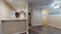 This single-floor unit offers a practical and well-appointed layout finished with rich, dark hardwood-style flooring and neutral warm-toned walls throughout. The open living area is illuminated by natural light from multiple windows fitted with blinds, and is equipped with a ceiling fan with integrated lighting. A textured ceiling adds a classic touch to the space, while clean white baseboards provide a crisp contrast to the flooring.

The galley-style kitchen is efficiently designed with dark cabinetry, granite-look countertops, and a decorative tile backsplash. It is equipped with a stainless steel refrigerator, an electric range, and a dishwasher. A window above the sink area brings in natural light, enhancing the functionality of the workspace. Track lighting overhead ensures the kitchen is well-lit. A half-wall with a breakfast bar connects the kitchen to the main living space, creating an open and accessible flow between areas.

The bathroom features a full-size soaking tub with a tiled surround and chrome fixtures, a toilet, and a vanity with dark wood cabinetry. The space is finished with the same hardwood-style flooring found throughout the unit, maintaining a cohesive aesthetic. Additional storage is accessible via a closet off the main living area, contributing to the overall functionality of this thoughtfully designed space.
