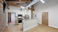 Located in Akron's Furnace Street district, this thoughtfully designed loft unit showcases a compelling blend of industrial heritage and contemporary renovation. Exposed original brick walls, dark ceiling beams, and large-diameter ventilation ductwork preserve the building's historic character, while light wood-tone flooring, crisp white trim, and modern fixtures create a clean, updated aesthetic throughout.

The galley-style kitchen is well-appointed with stainless steel appliances — including a range, microwave, and refrigerator — complemented by light wood cabinetry, white quartz countertops, a double-basin sink, and a tile backsplash. Sleek pendant lighting illuminates the workspace. The open living area features soaring ceilings with exposed structural beams, an arched brick window, and industrial-style pendant lighting, lending a spacious, loft-like ambiance.

The bathroom offers a full tub-shower combination with subway tile surround and chrome fixtures, finished with neutral tones for a clean, classic look. A dedicated laundry area houses a front-loading washer/dryer unit with vented exhaust. The closet space features full-height bi-fold doors and neutral carpeting, maximizing storage efficiency. This unit is ideal for those seeking urban character paired with practical, modern amenities.