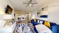 This thoughtfully designed 2-bedroom, 2-bathroom single-floor residence offers a generous and functional layout across a comfortable footprint. The open-concept living, dining, and kitchen area serves as the heart of the home, featuring light wood-look flooring, a ceiling fan, and direct access to a private balcony through glass-paned French doors that invite abundant natural light. The kitchen is outfitted with crisp white cabinetry, a white subway tile backsplash, stainless steel appliances including a full-size refrigerator and dishwasher, under-cabinet lighting, track and pendant lighting, and a rounded center island with bar seating — ideal for both casual dining and entertaining. The primary bedroom is a spacious retreat with plush carpeting, a ceiling fan, and a walk-in closet featuring multi-rod hanging storage on both sides. The second bedroom offers carpeted flooring, a ceiling fan, and a bright window. Both bathrooms are finished with light tile flooring and clean, neutral fixtures, with one featuring a full soaking tub and shower combination. Additional highlights include a dedicated laundry area, utility room, hallway, and two closets, rounding out a well-organized and comfortable living space.