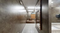 Located at 246–276 Kyser Blvd in Madison, Alabama, this well-appointed facility is a single-floor space designed to serve as a locker room and shower area. The interior makes a strong aesthetic impression through its rich, dark faux-finish walls that lend a sophisticated, moody ambiance throughout.

The layout flows from an entry corridor with light tile flooring into a main locker room area. The corridor features decorative wall sconces and a large framed mirror, creating a welcoming transition into the space. The locker room area is equipped with a set of metal lockers for secure storage and includes raised, cushioned bench seating upholstered in a textured crocodile-print fabric, providing a comfortable area for changing. A round leather ottoman adds to the functional yet stylish furnishings. A window with bamboo blinds allows for natural light while maintaining privacy.

Beyond the locker area, a dedicated shower zone features multiple private shower stalls enclosed with frosted glass sliding doors and chrome hardware, ensuring both privacy and ease of use. Circular mirror wall art decorates the shower area, reinforcing the space's cohesive design aesthetic. Overhead fluorescent lighting illuminates all areas uniformly. The textured ceiling and tile flooring throughout are practical and easy to maintain, making this a well-balanced blend of form and function.