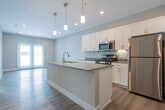 Located at 1700 Harmony Lake Dr in Muskegon, Michigan, this single-floor residence offers a thoughtfully designed layout with modern finishes and a cohesive, contemporary aesthetic. The open-concept kitchen serves as the heart of the home, showcasing white shaker-style cabinetry, stainless steel appliances including a gas range, microwave, and refrigerator, and a large central island with a built-in sink and light countertops. Pendant lighting above the island adds a stylish focal point, while warm wood-tone luxury vinyl plank flooring extends throughout the main living and kitchen areas, enhancing the bright, airy feel of the space. The bedrooms are finished with soft, neutral-toned carpet and feature windows with blinds that allow natural light to filter in. One bedroom includes a walk-in closet with built-in shelving, providing ample storage. The bathroom is well-appointed with a white vanity, light countertops, hardwood-style flooring, and a full tub-shower combination with clean white surround. Throughout the residence, neutral gray walls, white trim, and recessed lighting create a clean, move-in-ready environment that balances comfort and modern design.