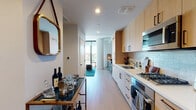 Located in the heart of Hollywood at 1755 Argyle Ave, this contemporary single-floor residence offers a thoughtfully designed layout with high-end finishes throughout. The galley-style kitchen is a standout feature, outfitted with light wood cabinetry, a subway tile backsplash, stainless steel appliances including a gas cooktop, built-in oven, and over-the-range microwave, all complemented by clean white countertops and light hardwood flooring that extends throughout the living areas. The open living space is anchored by dramatic floor-to-ceiling windows and glass balcony doors that bathe the room in natural light and frame sweeping views of the Hollywood skyline, palm trees, and surrounding cityscape. A private balcony extends the living area outdoors, perfect for taking in the Los Angeles scenery. The bedroom is a calm, well-proportioned retreat with soft, neutral tones and ample wall space. The bathroom features a frameless glass walk-in shower with stone mosaic tile walls and dark floor tile, paired with a light wood vanity and white countertop, delivering a clean, spa-like aesthetic. Light hardwood floors, recessed lighting, and a cohesive modern design palette unify the entire space.