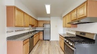 This single-floor residence at Woodbridge Terrace Apartments offers a thoughtfully designed layout with functional living spaces throughout. The galley-style kitchen serves as a central highlight, featuring warm honey-toned cabinetry, dark granite countertops, a tile backsplash, and stainless steel appliances including a gas range, refrigerator, and dishwasher. Light wood-style flooring runs throughout the kitchen, enhancing its clean, practical aesthetic.

The living areas are generously sized, finished with neutral carpeting and bright white walls that create a versatile backdrop. Sliding glass doors in the main living space open to an outdoor area, allowing natural light to flow in. Additional windows fitted with roller shades provide outdoor views and further illuminate the interior.

Bedrooms are carpeted and well-proportioned, with at least one room offering dual closets equipped with built-in shelving and hanging rods, providing substantial storage capacity. The bathrooms are neatly appointed, with one featuring a tub and shower combination accented by marble-style surround tiles and chrome fixtures, while another includes granite countertops and a framed mirror.