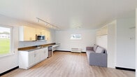 Located at 4711 University Ave in Cedar Falls, Iowa, this efficiently designed studio unit offers a smart, single-floor layout that maximizes every square foot. The open-plan living area features light wood-style vinyl flooring that flows throughout the space, creating a bright and cohesive feel. A large window invites natural light into the main living zone, which includes a wall-mounted Murphy bed with built-in overhead cabinetry, a sliding barn-door closet with gold hardware, and a wall-mounted HVAC unit for year-round comfort.

The kitchen runs along one wall and is well-appointed with white shaker-style cabinetry, gold and brushed-nickel hardware, a stainless steel countertop with an undermount sink, a compact refrigerator, a stainless steel microwave, and a built-in desk area — ideal for studying or working from home. Track lighting overhead provides ample task illumination.

The bathroom is clean and functional, finished in crisp white with light wood-style flooring, a soaking tub with shower, a white vanity with a dark countertop, a large mirror, and a bright vanity light. The overall aesthetic of the unit is modern and minimalist, with a neutral palette that lends itself to easy personalization.
