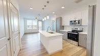 Located at 5750 Airport Rd in Santa Fe, NM, this modern 2-bedroom, 4-bathroom residence offers a thoughtfully designed single-floor layout with clean, contemporary finishes throughout. The open-concept kitchen serves as the centerpiece of the home, showcasing a large white waterfall island with an undermount sink, two-tone cabinetry pairing white upper shaker cabinets with gray lower cabinets, a marble-style tile backsplash, and a full suite of stainless steel appliances including a refrigerator, range, and over-the-range microwave. Pendant lighting over the island adds a warm, modern touch. The kitchen flows seamlessly into the living area, which features light hardwood flooring, a ceiling fan, and a glass door leading to an outdoor space with natural views. The bedrooms are finished with plush carpet and receive natural light through large windows. The primary bedroom connects to a well-appointed en-suite bathroom featuring a dual-sink vanity with gray cabinetry, a glass-enclosed walk-in shower, and direct access to a spacious walk-in closet with built-in shelving and hanging rods. A second full bathroom offers a soaking tub and additional closet access. The home's bright, neutral palette and modern fixtures create a clean, inviting ambiance throughout.