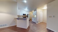 Located at 1318 Mossy Ln in Mishawaka, Indiana, this two-floor residence offers a well-designed layout with a variety of functional living spaces. The main level centers around an open-concept kitchen and living area, where vaulted ceilings lend a sense of spaciousness and height. The kitchen is outfitted with white shaker-style cabinetry, granite-look countertops, and a full suite of stainless steel appliances including a gas range, microwave, and refrigerator. A peninsula with bar seating connects the kitchen to the adjacent living and dining areas, which feature durable hardwood-style flooring throughout. A pendant light fixture adds a decorative accent near the dining space. The bedrooms are carpeted and generously sized, with one featuring vaulted ceilings and a large window that allows natural light to fill the room. The bathroom includes a granite-topped vanity with white cabinetry, a soaking tub with white tile surround, and hardwood-style flooring, with an adjacent walk-in closet providing ample storage. The lower level contains an unfinished basement with concrete floors and exposed framing, offering substantial potential for additional living or storage space.