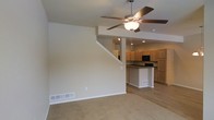 This well-designed residential space is spread across three floors, offering a versatile and functional layout suited for everyday living. The main level showcases an open-concept design where the living area flows seamlessly into the kitchen, creating an inviting and connected space. The living area features neutral-toned carpet flooring, soft beige walls, and a ceiling fan with integrated lighting, contributing to a comfortable and airy ambiance. Recessed lighting further enhances the brightness of the space.

The kitchen is equipped with light wood cabinetry, a dark countertop island that serves as a natural dividing point between the cooking and living areas, and black appliances including a built-in microwave. The hard surface flooring in the kitchen provides a practical contrast to the carpeted living space.

A staircase visible from the main living area connects the floors, underscoring the multi-level nature of the home. The consistent use of neutral tones — from the walls to the flooring — creates a cohesive and clean aesthetic throughout. The open layout and thoughtful design of the main level make it an ideal setting for both everyday living and entertaining, while the additional floors offer further space and privacy.