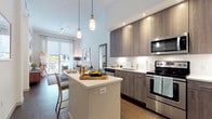 This single-floor residence showcases a thoughtfully designed open-concept layout that integrates the living, dining, and kitchen areas into one cohesive space. Dark hardwood flooring runs throughout the main living areas, providing a warm contrast to the bright white walls and ceilings. The living room features a large sliding glass door that allows abundant natural light and opens to an outdoor balcony with views of surrounding greenery. A dedicated dining area accommodates a round wood table with seating for four, while the kitchen is equipped with stainless steel appliances, textured wood cabinetry, recessed lighting, pendant lights, and a breakfast bar with seating for two.

The bedroom is a calm retreat with a window dressed in sheer curtains, dark hardwood floors, and ample space for a full bedroom suite. It connects directly to a luxurious primary bathroom finished in marble-style tile throughout. The bathroom features a dual-sink vanity with dark wood cabinetry, a large wall mirror, and a generously sized glass-enclosed shower and soaking tub combination clad in striking marble-veined tile. A walk-in closet with built-in shelving provides practical storage adjacent to the bathroom, completing the well-organized layout.