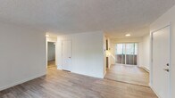 Located at 19705 SW Boones Ferry Rd in Tualatin, Oregon, this single-floor unit offers a clean, well-maintained layout with a bright and neutral aesthetic throughout. The open living and dining areas are finished with light wood-style laminate flooring that extends through the main spaces, complemented by textured ceilings and crisp white walls that enhance the sense of openness. Large windows dressed with vertical blinds allow generous natural light to filter in while offering views of the surrounding greenery. Baseboard heating is present throughout, providing efficient warmth across the unit. The kitchen features grey cabinetry, white countertops, a stainless steel refrigerator, and sliding panel doors that conceal additional storage, making it both functional and tidy. The bedroom is carpeted for comfort and includes a ceiling fan, a wide sliding-door closet, and a window framing lush outdoor tree views. The bathroom is outfitted with a full tub-shower combination, a curved shower rod, wood-style tile flooring, and a vanity with ample counter space. The overall layout is practical and efficiently organized, offering a comfortable living environment in a well-connected Tualatin location.