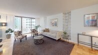 Located in the heart of Bethesda, MD, this thoughtfully designed single-floor residence blends contemporary style with warm, eclectic touches throughout. The entry hallway sets an immediately distinctive tone, featuring a textured metallic accent wall, an oversized arched gold-framed mirror, and curated artwork that establishes a chic, artistic atmosphere.

The spacious living room is anchored by light parquet hardwood flooring and flows seamlessly toward a wall of floor-to-ceiling sliding glass doors that open onto a private balcony, offering open urban views of the Bethesda skyline. Natural light fills the room generously, highlighting the neutral furnishings and a decorative wallpaper accent panel.

The dining area, nestled nearby, features its own textured accent wall and a bright window overlooking the city, creating an intimate yet airy setting for meals.

The kitchen is well-appointed with gray shaker cabinetry, white countertops, and stainless steel appliances including a gas range, microwave, and refrigerator — all finished in a clean, modern palette.

The bedroom is a bold and vibrant retreat, with a striking yellow feature wall, a reclaimed wood-style headboard, wide closets, and a large window that invites in natural light and city views. Warm hardwood flooring carries throughout, tying the entire residence together with a cohesive, welcoming aesthetic.