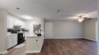Located at 6350 Oakley Rd in Union City, GA, this single-floor residence offers a well-designed, open-concept layout that balances comfort and functionality. The kitchen is a standout feature, showcasing crisp white cabinetry, light quartz-style countertops, a mosaic tile backsplash, and black and stainless steel appliances. A peninsula extends into the living area, creating a natural flow between cooking and entertaining spaces. The living room is generously sized, featuring rich hardwood-style flooring, a ceiling fan, and sliding glass doors that open to a private patio, filling the space with natural light and outdoor views. A dedicated dining area with wood-look flooring and an elegant pendant light provides a defined space for meals. The bedrooms are carpeted for comfort, each offering ceiling fans and natural light through window blinds. Storage is well-considered throughout, with a spacious walk-in closet featuring wire shelving and a separate linen closet adjacent to the bathroom. The bathroom includes white cabinetry, a large vanity mirror, and ample counter space. Textured ceilings and neutral gray tones throughout lend a clean, cohesive aesthetic to this move-in-ready home.