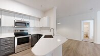 Located at 2424 E TC Jester Blvd in Houston, TX, this single-story, 2-bedroom, 4-bathroom residence offers a clean, modern aesthetic throughout its efficiently arranged floor plan. The open-concept kitchen and living area serves as the heart of the unit, anchored by a curved peninsula with white quartz countertops and an undermount sink. White shaker cabinetry, a subway tile backsplash, and stainless steel appliances—including a refrigerator, electric range, and microwave—complete the kitchen. Light wood-style flooring runs through the main living areas, creating a warm, cohesive feel. The living room is open and well-lit, with a mirrored accent wall adding visual depth. Both bedrooms feature soft carpet flooring and natural light from windows with blinds. The primary bedroom includes a ceiling fan and access to a walk-in closet with multi-level shelving and hanging rods. The bathrooms are finished with gray cabinetry, white quartz countertops, and framed mirrors, with at least one featuring a tub-shower combination. A dedicated laundry area accommodates a full-size washer and dryer, adding everyday convenience to this well-appointed residence.