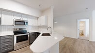 Located at 2424 E TC Jester Blvd in Houston, TX, this single-story, 2-bedroom, 4-bathroom residence offers a clean, modern aesthetic throughout its efficiently arranged floor plan. The open-concept kitchen and living area serves as the heart of the unit, anchored by a curved peninsula with white quartz countertops and an undermount sink. White shaker cabinetry, a subway tile backsplash, and stainless steel appliances—including a refrigerator, electric range, and microwave—complete the kitchen. Light wood-style flooring runs through the main living areas, creating a warm, cohesive feel. The living room is open and well-lit, with a mirrored accent wall adding visual depth. Both bedrooms feature soft carpet flooring and natural light from windows with blinds. The primary bedroom includes a ceiling fan and access to a walk-in closet with multi-level shelving and hanging rods. The bathrooms are finished with gray cabinetry, white quartz countertops, and framed mirrors, with at least one featuring a tub-shower combination. A dedicated laundry area accommodates a full-size washer and dryer, adding everyday convenience to this well-appointed residence.