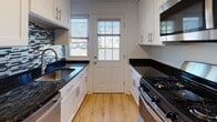 Located at 283 Cooper Pl in New Haven, CT, this three-floor property offers a clean, well-maintained interior defined by warm hardwood flooring that flows consistently throughout the living spaces. The main level features an open layout with white walls, crisp trim, and natural light admitted through multiple windows fitted with blinds. A staircase connects the floors, with a windowed landing that keeps the vertical circulation bright and airy.

The kitchen stands out as a highlight of the home, outfitted with white shaker-style cabinetry, dark granite countertops, a mosaic tile backsplash, stainless steel hardware, and a gas range. A rear door in the kitchen provides direct outdoor access.

The upper levels house several versatile rooms, each featuring hardwood floors, ceiling fans or flush-mount lighting, and windows that allow natural light to filter in. The bathroom is well-appointed with a soaking tub, gold-tone fixtures, and large-format wood-look tile surrounding the tub surround, complemented by a window for ventilation.

The basement level provides practical utility space with exposed structural elements, HVAC ductwork, gas line access, and a small ground-level window. This floor offers valuable storage or mechanical utility capacity. Throughout, the property maintains a consistent, neutral palette that is both functional and easy to personalize.