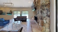 The Creekside clubhouse is a thoughtfully designed single-story community facility that combines functional amenities with inviting architectural details. At the heart of the main lounge, a striking floor-to-ceiling natural stone fireplace serves as the room's focal point, featuring a raised stone hearth and a wall-mounted television above. Vaulted ceilings with exposed beams enhance the sense of volume in this area, while large arched and sliding windows flood the space with natural light and provide direct views of the outdoor pool and surrounding greenery.

The lounge is furnished with leather sofas, a glass coffee table, and a patterned area rug, creating a comfortable gathering area. Adjacent to this space, a separate seating room displays a "Creekside" branded sign above horizontal clerestory windows, maintaining privacy while still allowing natural light.

The leasing and administrative area features light hardwood-style flooring, vaulted ceilings, pendant lighting, and a central consultation desk, with French doors opening to a formally arranged meeting room. A dedicated fitness center, visible through the 3D floorplan scan, is equipped with multiple cardio and strength machines, rounding out the facility's offerings for residents.
