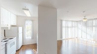 Located at 900 F Street in the heart of San Diego, Unit #233 is a single-floor residence designed with a clean, minimalist aesthetic throughout. The open-concept living area is one of the unit's standout features, showcasing rich hardwood flooring that runs throughout the main living spaces. Floor-to-ceiling vertical blinds line the corner windows, allowing an abundance of natural light to pour in from multiple directions, creating a bright and airy atmosphere. A ceiling fan with a light fixture adds both comfort and function to this sun-filled space. The kitchen is positioned at the heart of the unit, featuring a pass-through breakfast bar that opens to the living area. White cabinetry, under-cabinet lighting, and white appliances give the kitchen a clean, cohesive look. The bedroom offers plush wall-to-wall carpeting for added comfort and is equipped with a sliding-door closet, providing ample storage. The bathroom is finished with neutral tones, terrazzo-style countertops, and a framed mirror, maintaining the unit's consistent, understated design language. With its bright interiors, open layout, and warm wood floors, this unit offers a functional and welcoming living environment in a prime San Diego location.