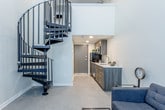 Located at 5522 Troost Ave in Kansas City, MO, this thoughtfully designed two-floor unit offers a clean, contemporary aesthetic with functional layout throughout. The main level greets you with soaring double-height ceilings that amplify the sense of openness and airiness in the living area. A striking black spiral staircase serves as both a functional element and a bold architectural focal point, connecting the two floors with style. The living area is bright and welcoming, with a large window that invites natural light to fill the space. The kitchen runs efficiently along one wall, featuring dark wood cabinetry with modern hardware, light countertops, stainless steel appliances including a microwave, refrigerator, and dishwasher, and a clean subway tile-style backsplash. A galley-style entry corridor leads to a secure entry door, keeping the living and kitchen areas uncluttered. Ascending the spiral staircase, the upper loft level provides a versatile open space complete with a wall-mounted mini-split HVAC unit and a railing overlooking the lower floor, making it ideal for use as a sleeping or working area. The bathroom is finished with crisp white subway tile surrounding a full soaking tub, a modern floating vanity, and a mirrored medicine cabinet, creating a clean and polished feel throughout.