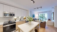 Located at 1650 NE 124th St in North Miami, FL, this well-appointed three-bedroom, two-bathroom residence offers a thoughtfully designed single-floor layout. The open-concept kitchen, dining, and living area forms the heart of the home, bathed in natural light from large floor-to-ceiling grid-style windows and sliding glass doors that frame lush palm tree and pool views. The kitchen is outfitted with sleek two-tone cabinetry in white gloss and warm tan, a subway tile backsplash, stainless steel appliances, white quartz countertops, and a central island with bar seating. The living room features warm hardwood flooring, track lighting, and direct access to the outdoor balcony. The primary bedroom offers a bold accent wall and a dedicated closet, while each bedroom benefits from its own closet space. The two bathrooms showcase marble-look porcelain tile throughout; the primary bath includes a frameless glass walk-in shower, while the second bath features a full tub-shower combination with elegantly veined wall surround. A hallway connects the private quarters, with additional closets providing generous storage. The overall ambiance is bright, clean, and contemporary throughout.