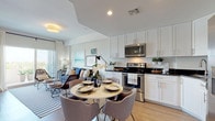 This well-designed single-floor residence offers a seamless open-concept layout that connects the kitchen, dining, and living areas into one cohesive and functional space. The kitchen is outfitted with crisp white shaker cabinetry, dark stone countertops, and a full suite of stainless steel appliances, including a range, microwave, dishwasher, and a large side-by-side refrigerator. A round dining table sits just off the kitchen, creating a natural transition into the dining area. The living room is bright and airy, featuring sliding glass doors that open to a private balcony with open outdoor views, allowing abundant natural light to fill the space. Light wood-style flooring runs throughout the main living areas, contributing to a clean and contemporary aesthetic. The bedrooms are comfortably sized, each featuring large windows with blinds and sheer curtains that allow for flexible light control, along with dedicated workspace areas. The bathrooms are finished with large-format neutral stone-look tile, with one bathroom featuring a soaking tub and tiled surround, and another offering a walk-in shower with full tile walls. Overall, the residence combines modern finishes with a relaxed, coastal-inspired ambiance.