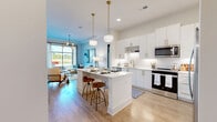 Located at 525 Sawnee Village Boulevard in Cumming, GA, this 1-bedroom, 1-bathroom residence offers a thoughtfully designed open-concept floor plan with contemporary finishes throughout. Light hardwood-style flooring flows through the main living areas, creating a bright and cohesive aesthetic.

The kitchen is a standout feature, boasting floor-to-ceiling white cabinetry with gold hardware, a textured tile backsplash, stainless steel appliances including a French door refrigerator and gas range, and a central island with a quartz countertop and bar seating — all illuminated by elegant pendant lighting.

The living room is anchored by a large picture window that floods the space with natural light and provides views of the surrounding community. A tray ceiling with a modern multi-bulb chandelier adds architectural character.

The bedroom offers a comfortable, well-proportioned retreat with plush carpet, a decorative wall panel feature, and large windows with outdoor views. A dedicated closet provides practical storage.

The bathroom is clean and modern, featuring a gray vanity with white countertop, a framed mirror, and a full soaking tub with tile surround. Every room reflects a consistent, contemporary design sensibility ideal for modern living.