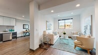 Located at 552 N Hobart Blvd in the heart of Los Angeles, this modern single-floor residence offers a thoughtfully designed open layout with clean lines and contemporary finishes throughout. The living room is bright and welcoming, featuring warm hardwood-style flooring, recessed lighting, and large black-framed windows that invite generous natural light and neighborhood views. Structural columns add an architectural dimension to the open-plan living and dining areas, which flow seamlessly into one another. The dining area comfortably accommodates a round glass-top table and is framed by a large window overlooking the surroundings. The kitchen is a standout feature, boasting high-gloss upper cabinetry, dark wood-toned lower cabinets, a sleek tile backsplash, white quartz countertops, and a full suite of stainless steel appliances. The bedroom is a serene retreat, carpeted for comfort and lined with multiple windows on two walls, filling the space with light and offering views of the neighborhood's palm tree-dotted skyline. The bathroom is finished with marble-look tile flooring, a dark wood vanity with a white countertop, a framed mirror, and dark pivot doors, lending a sophisticated, modern aesthetic throughout.